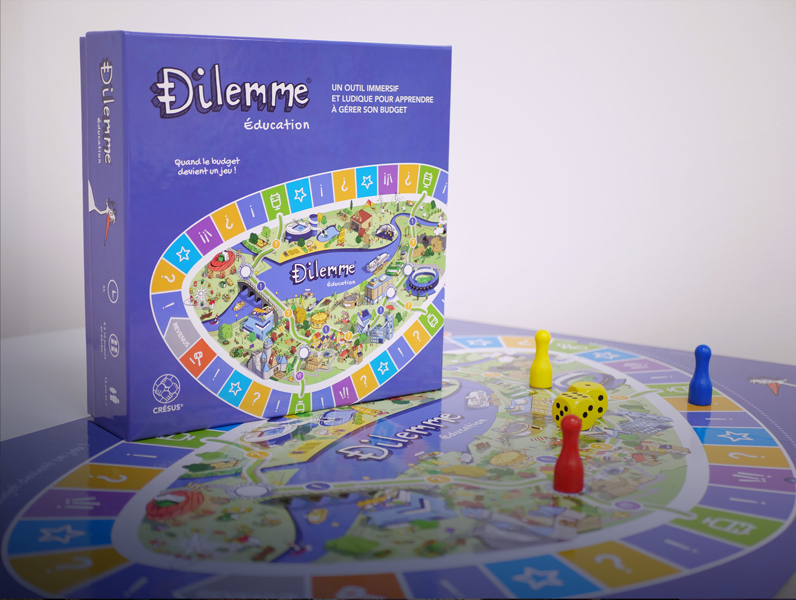 Boîte du jeu « Dilemme Éducation » posée à gauche sur un plateau de jeu illustré. Sur le plateau, trois pions , rouge, jaune, bleu et deux dés jaunes sont visibles au premier plan. Fond gris clair.